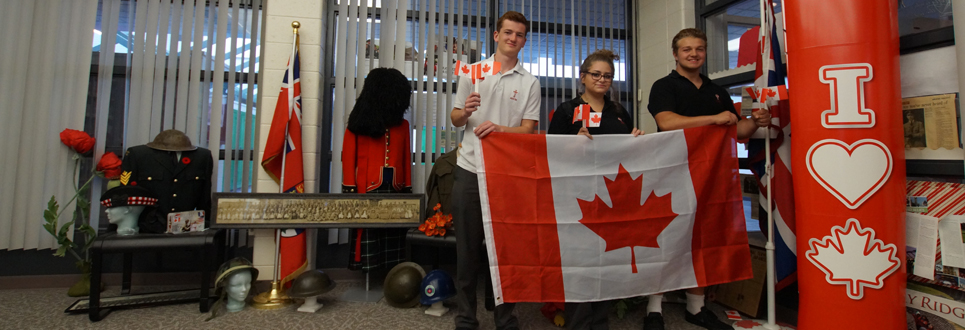 Students holding Canadian flag standing by World War display